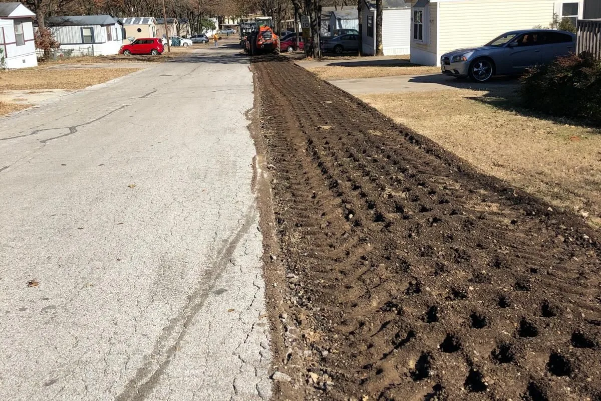A residential street being rebuilt in place — half asphalt, half churned road base ready for LL-TEQ integration. The materials you already own become the road.